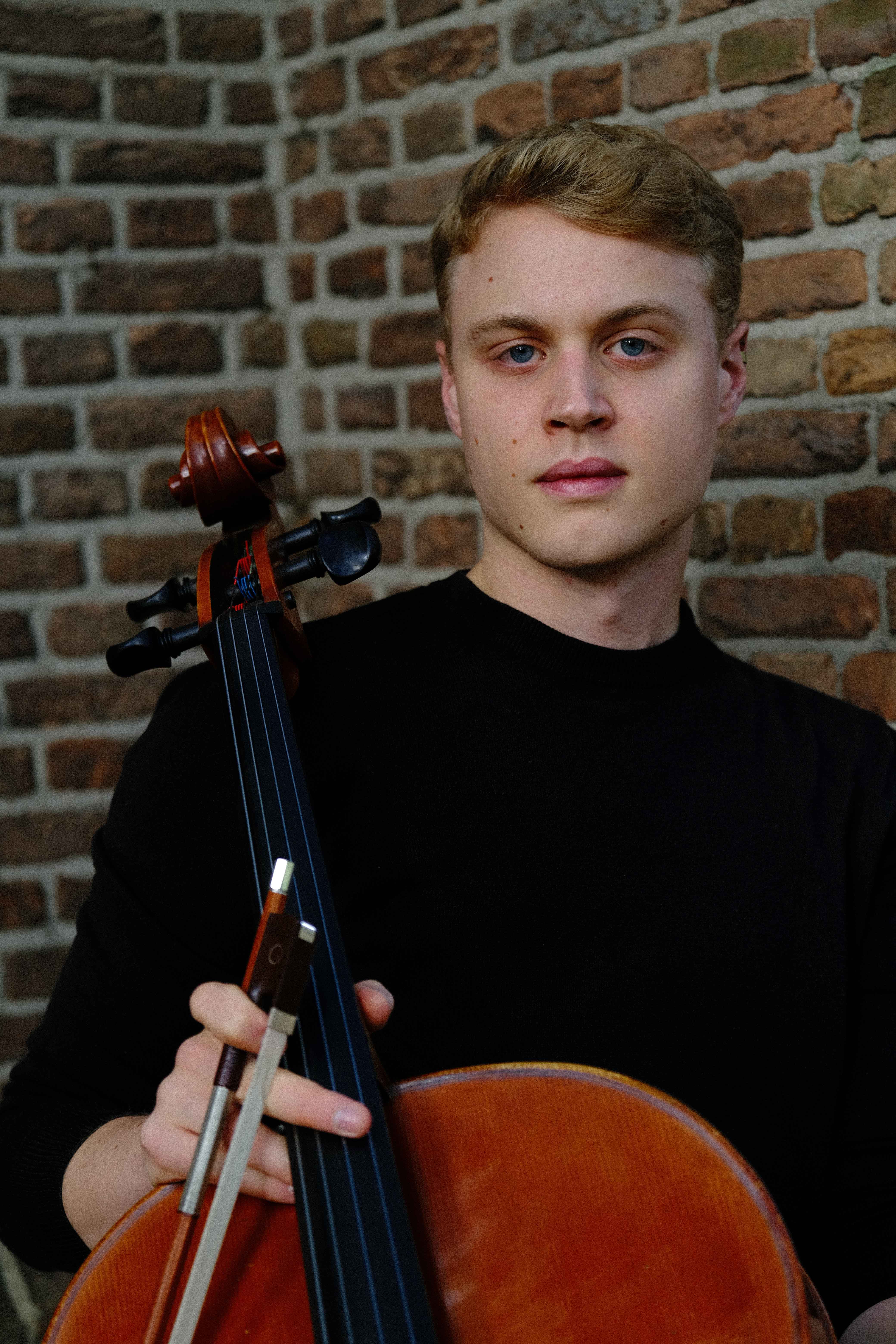 Luka Stefanović full-body with cello against historic architecture, The Hague